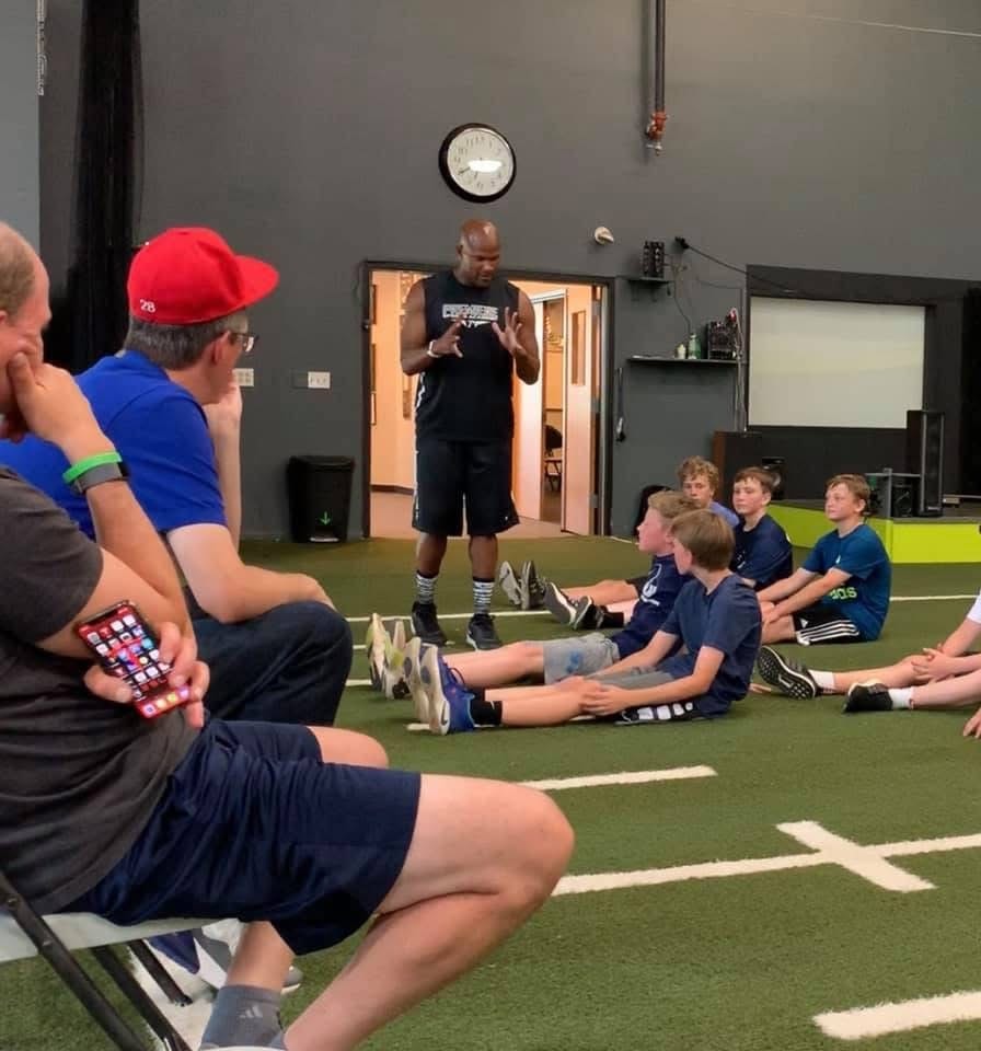 Antonio Davis speaking to seated youth athletes and parents at the training center