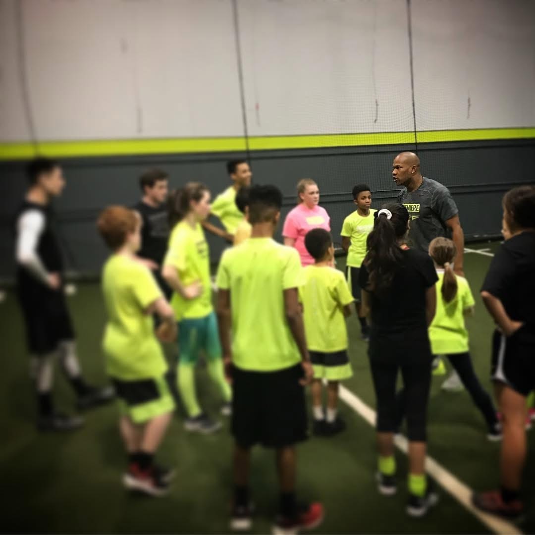 Antonio Davis addressing a large group of youth athletes in neon jerseys