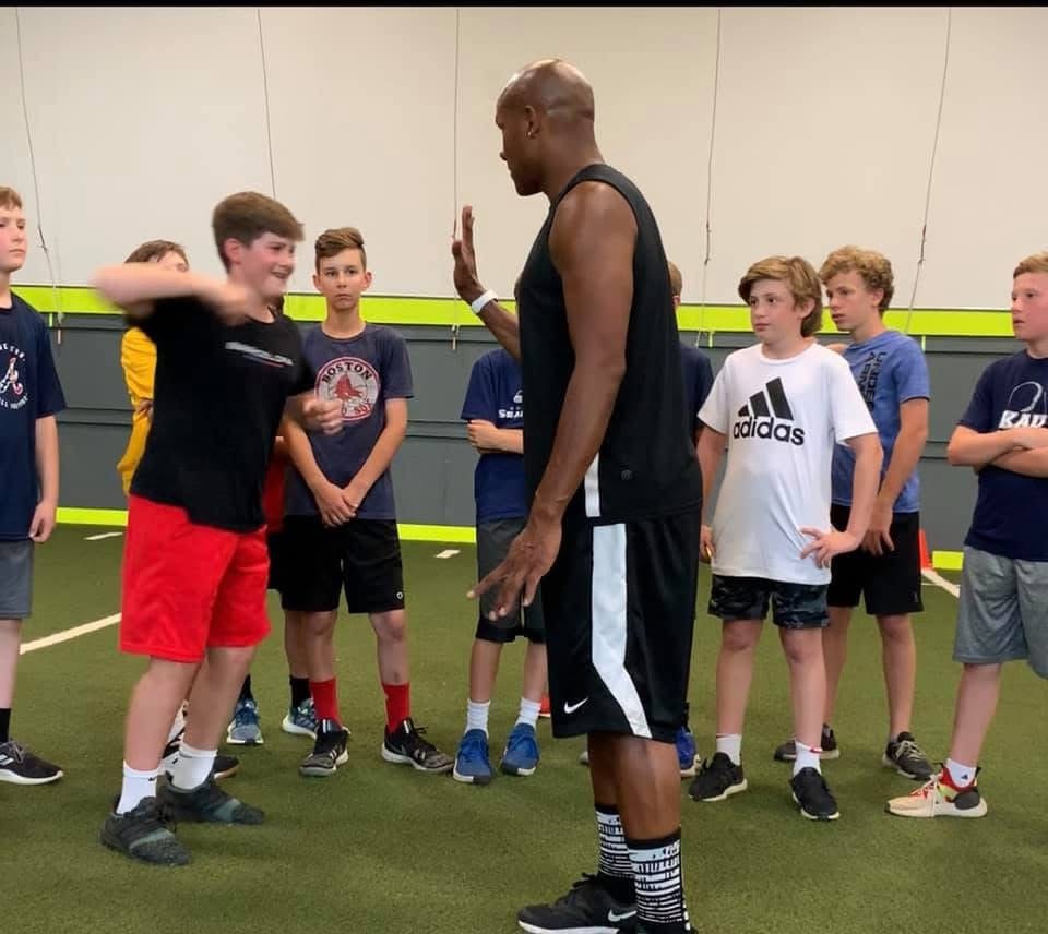 Antonio Davis working one-on-one with a youth athlete surrounded by a group